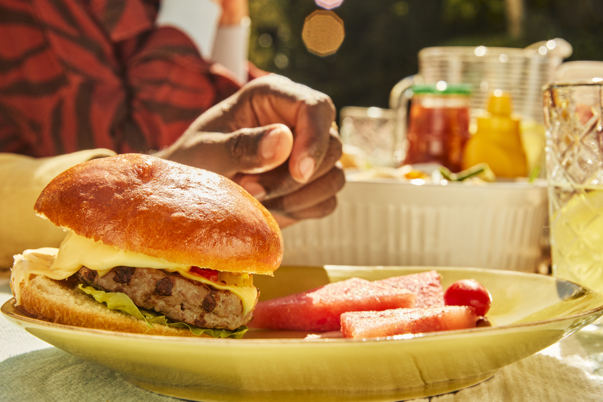 Turkey burger and fruit on a yellow plate outside.