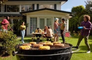 Friends enjoying a backyard barbecue with burgers on the grill.